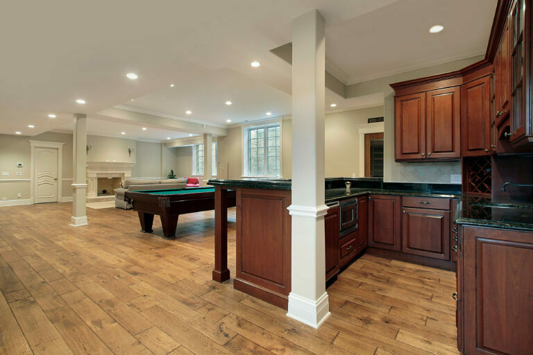 basement remodel with wood floor kitchenette white pillar recessed lighting and a fireplace with a pool table